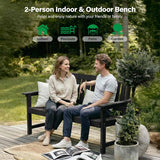 Two people sitting on a 2-person indoor & outdoor bench in a garden setting.