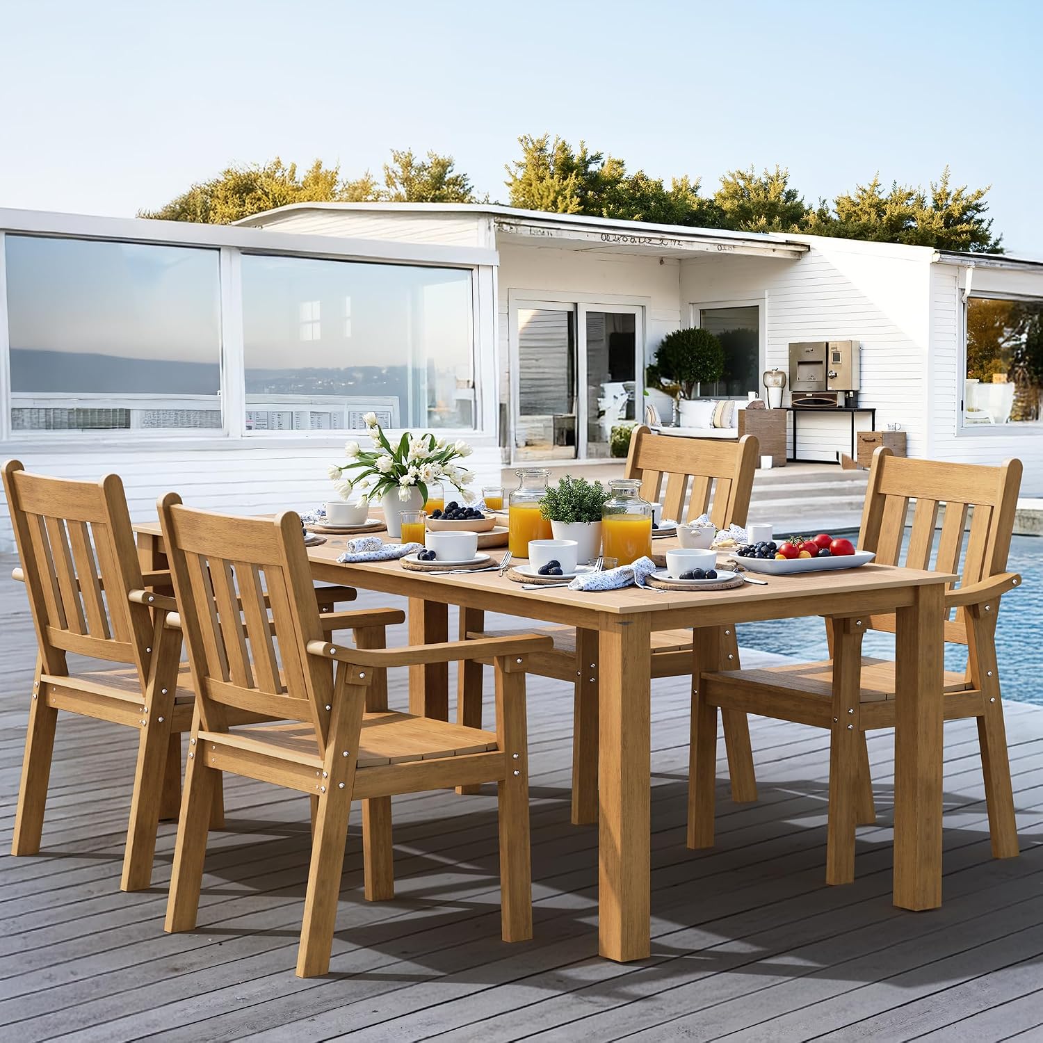 Wooden outdoor dining set with table and chairs on a deck, featuring a modern house and pool in the background.